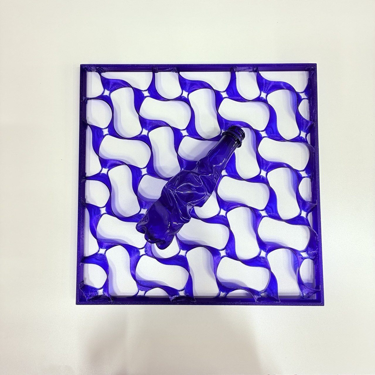 Top-down view: a purple TacTile lattice with a crushed PET bottle in the same color resting on top — input and output side by side